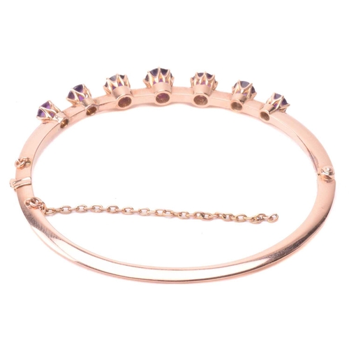 137 - A late Victorian amethyst hinged bangle, set with a row of four amethysts and three purple paste, to... 
