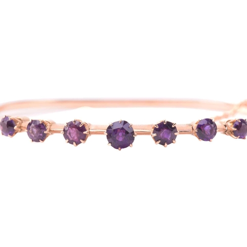 137 - A late Victorian amethyst hinged bangle, set with a row of four amethysts and three purple paste, to... 