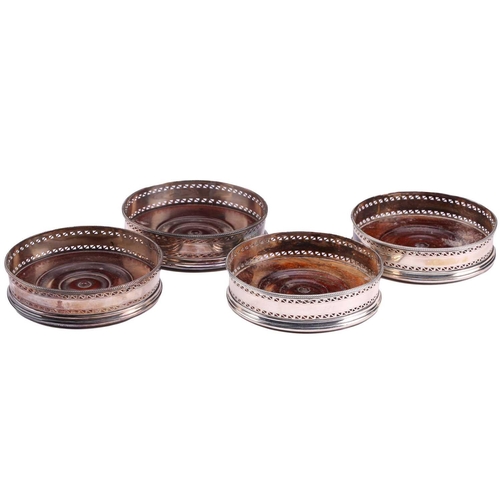 531 - A set of four George III silver mounted wine coasters; circular with beaded borders, pierced zig-zag... 
