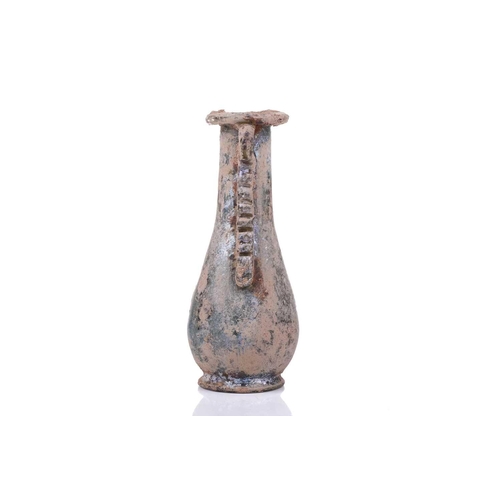 255 - A Roman glass oil flask with a pair of applied ribbon form handles and everted rim over an inverted ... 