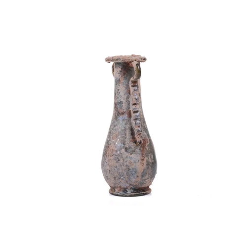 255 - A Roman glass oil flask with a pair of applied ribbon form handles and everted rim over an inverted ... 