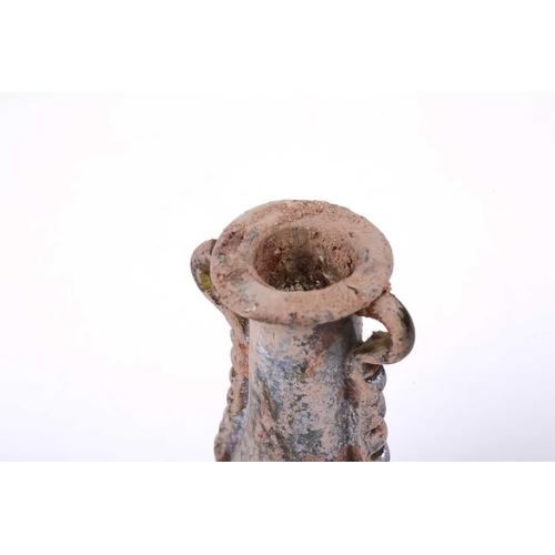 255 - A Roman glass oil flask with a pair of applied ribbon form handles and everted rim over an inverted ... 