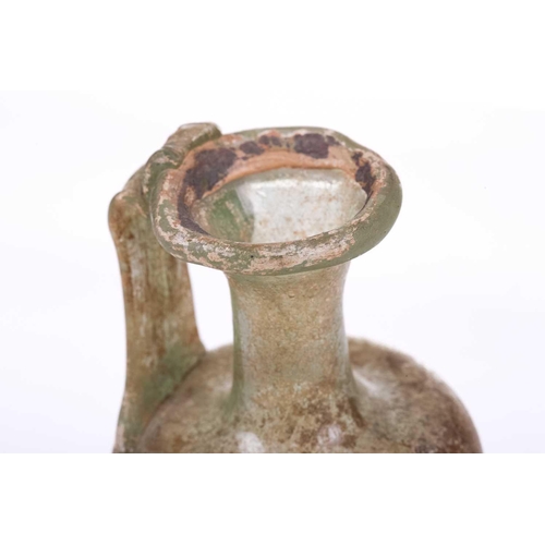 261 - A Roman glass oil ewer of slightly perpendicular form with moulded strap handle to the everted rim, ... 