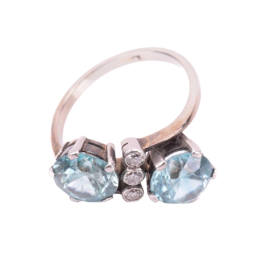 117 - A blue zircon and diamond cross-over ring, comprising two circular zircons of 8.0 mm in claw setting... 