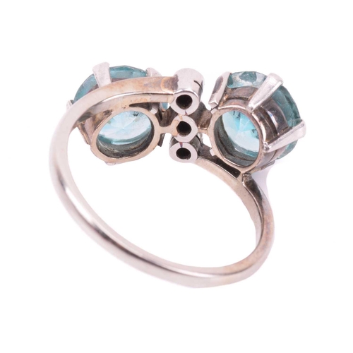 117 - A blue zircon and diamond cross-over ring, comprising two circular zircons of 8.0 mm in claw setting... 