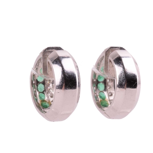 132 - A pair of emerald and diamond 'huggy' hoop earrings, both set with a central row of round cut emeral... 