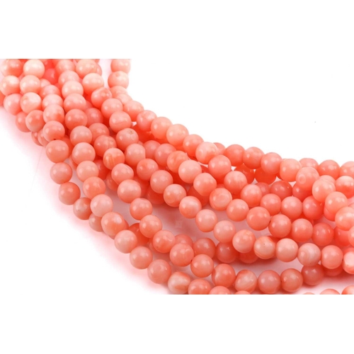 159 - A pink coral torsade necklace and earrings en-suite; the necklace contains nine rows of pink coral b... 