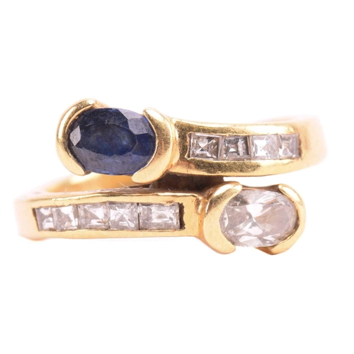 297 - A diamond and sapphire crossover ring, featuring an oval-cut diamond and a sapphire in collet settin... 