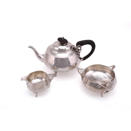 492 - An Art Nouveau three piece tea set, circular spot hammered; the teapot with commemorative engraving ... 