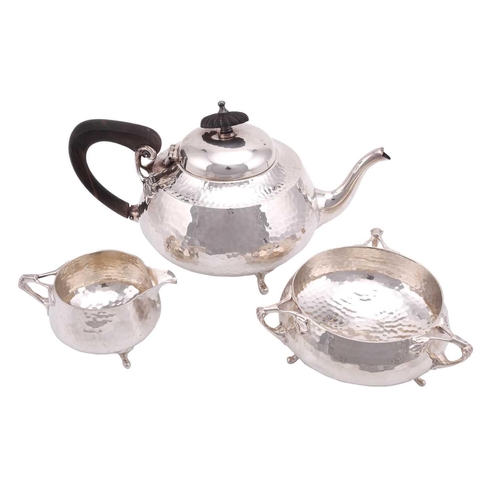 492 - An Art Nouveau three piece tea set, circular spot hammered; the teapot with commemorative engraving ... 