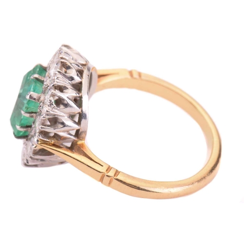 7 - An emerald and diamond cluster ring; the central rectangular step-cut emerald measuring approximatel... 