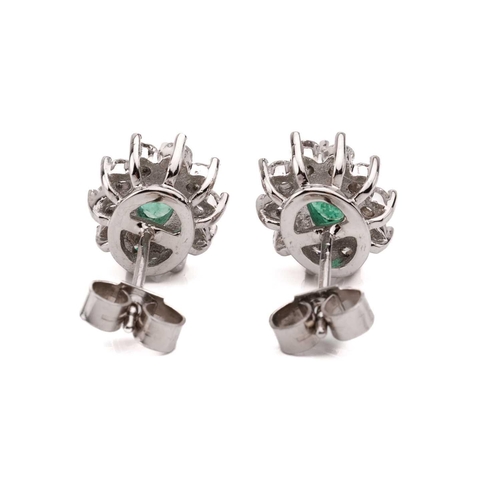 14 - A pair of 18 carat white gold, emerald and diamond earrings; the oval cut emeralds in claw mounts wi... 