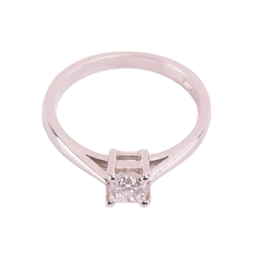 23 - A single stone diamond ring; the princess diamond in four claw mount, to tapered shoulders and plain... 