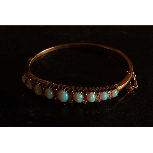 38 - A Victorian opal and diamond hinged bangle, the bracelet features a graduated row of nine oval caboc... 