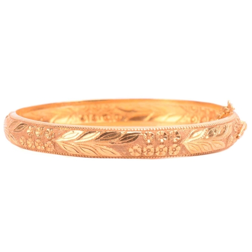 77 - A floral hinged bangle, with engraved foliate decorations and beaded borders, fastens with a push cl... 