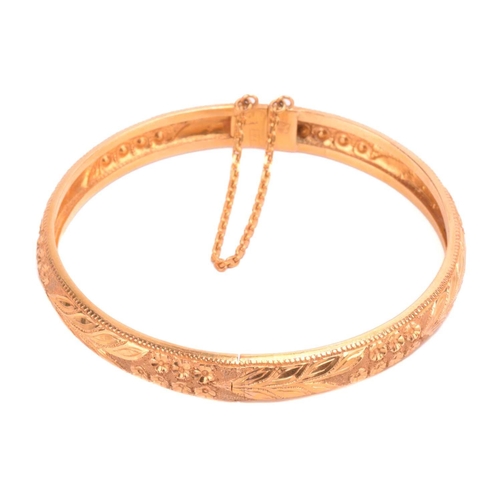 77 - A floral hinged bangle, with engraved foliate decorations and beaded borders, fastens with a push cl... 