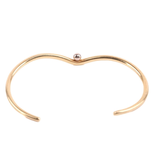 79 - An open bangle of undulating design, flush-set with a single diamond accent, yellow metal stamped '7... 