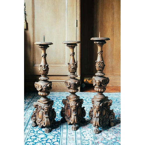 144 - Three similar 18th-century softwood carved altar candlesticks, formerly gilt, on three lion paw feet... 