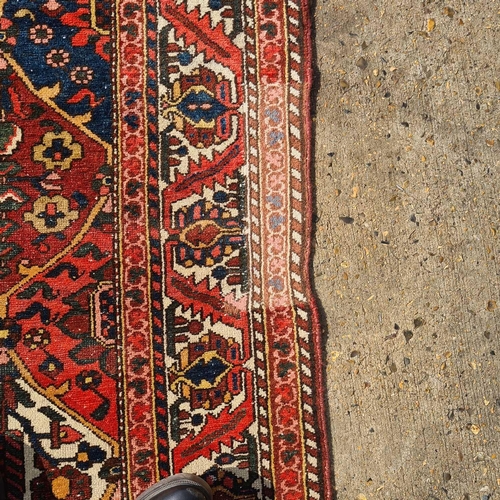 165 - A red ground Baktiari carpet, with an allover compartmented design within multiple borders, 302 cm x... 