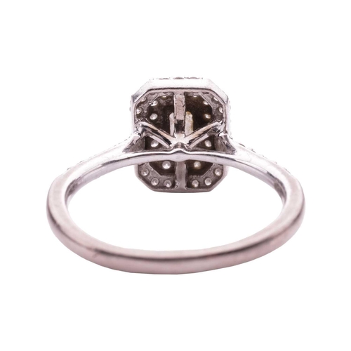 111 - A diamond cluster ring, featuring an emerald cut diamond within a two row border of round brilliant ... 