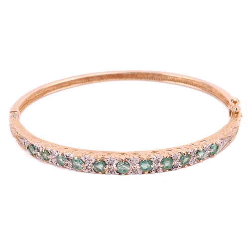 78 - An emerald and diamond bangle, set with a row of round emeralds interspersed with single cut diamond... 