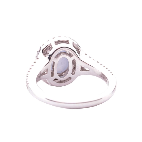 100 - A star sapphire and diamond cluster ring in 18ct white gold, centred with an oval star sapphire cabo... 