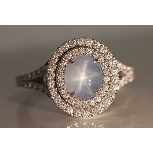 100 - A star sapphire and diamond cluster ring in 18ct white gold, centred with an oval star sapphire cabo... 