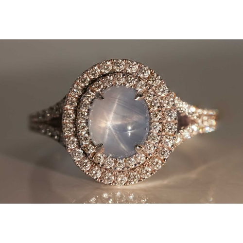 100 - A star sapphire and diamond cluster ring in 18ct white gold, centred with an oval star sapphire cabo... 