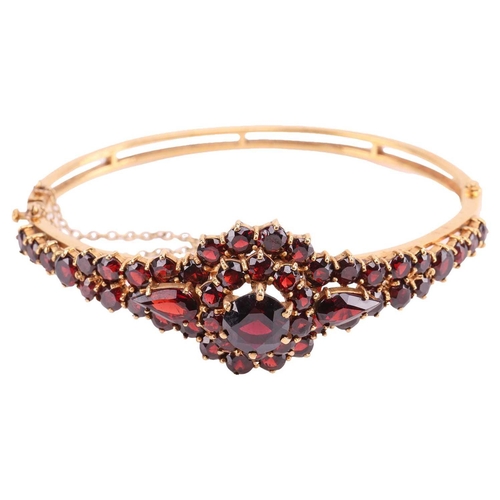 19 - A garnet-set bangle, of floral design, set with graduated round and pear-shaped garnets, to a 9ct go... 