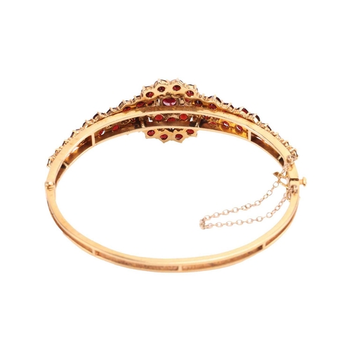 19 - A garnet-set bangle, of floral design, set with graduated round and pear-shaped garnets, to a 9ct go... 