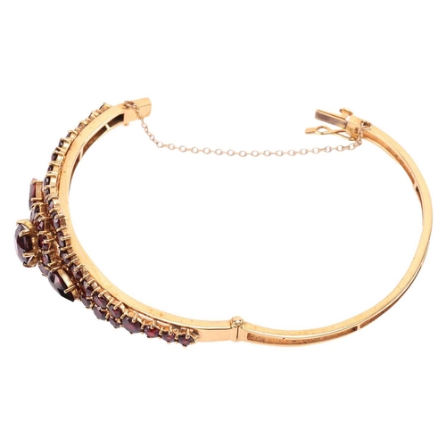 19 - A garnet-set bangle, of floral design, set with graduated round and pear-shaped garnets, to a 9ct go... 