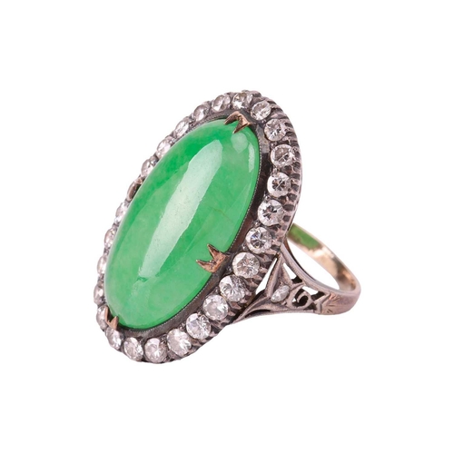 44 - A jade and diamond halo ring, featuring an elongated oval jadeite cabochon of yellowish-green colour... 