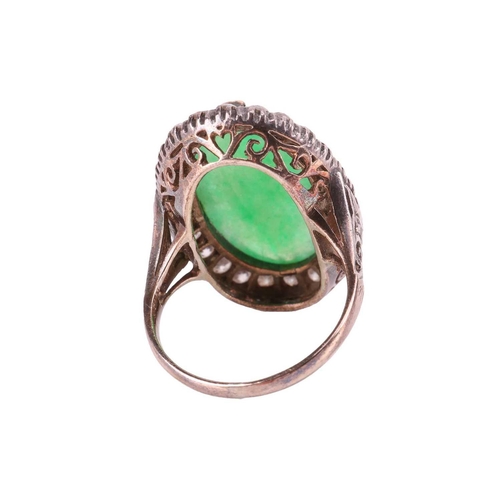 44 - A jade and diamond halo ring, featuring an elongated oval jadeite cabochon of yellowish-green colour... 