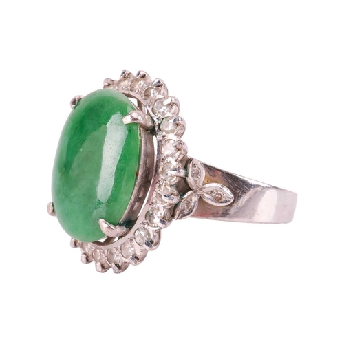 94 - A jade and diamond halo ring, comprising an oval jadeite cabochon of deep green colour, approximatel... 