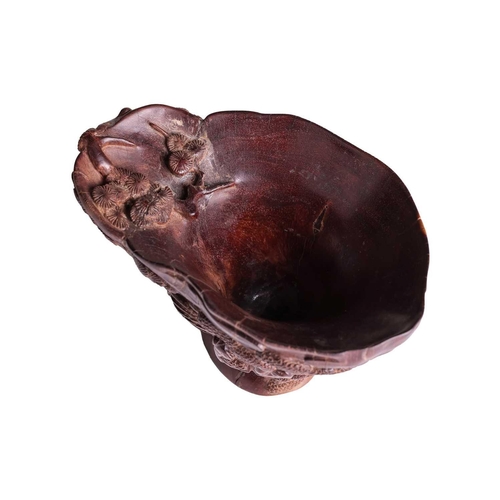 71 - A Chinese hardwood libation cup, carved to resemble a rhinoceros horn, the body decorated in relief ... 