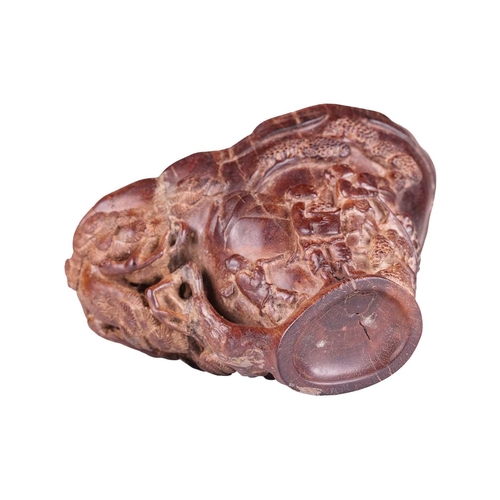71 - A Chinese hardwood libation cup, carved to resemble a rhinoceros horn, the body decorated in relief ... 