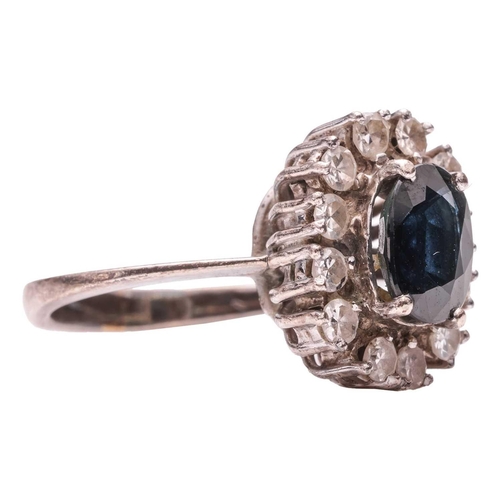 251 - A sapphire and diamond cluster ring, claw-set with an oval-cut sapphire of dark blue colour, approxi... 