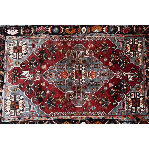 144 - A plum-coloured ground Baktiari rug with a central diamond lozenge, within a dark indigo geometric b... 