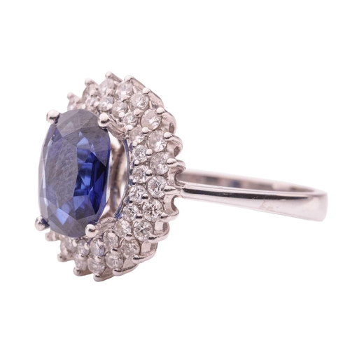 36 - A synthetic sapphire and diamond cluster ring, comprising a central claw-set oval-cut synthetic sapp... 