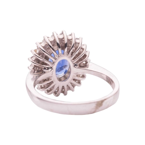 36 - A synthetic sapphire and diamond cluster ring, comprising a central claw-set oval-cut synthetic sapp... 