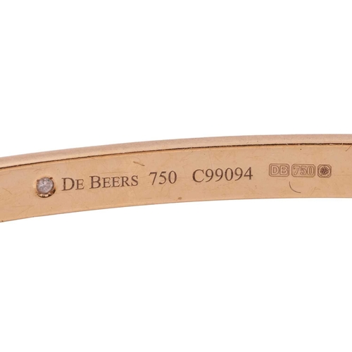 56 - De Beers - a hinged bangle in 18ct yellow gold, featuring a polki diamond gypsy-set to the front, th... 