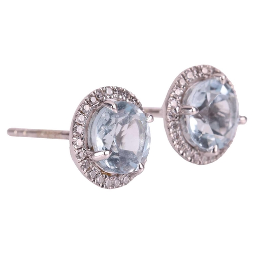 76 - Blue topaz and diamond stud earrings, each featuring a central claw set round-cut blue topaz of 6mm,... 