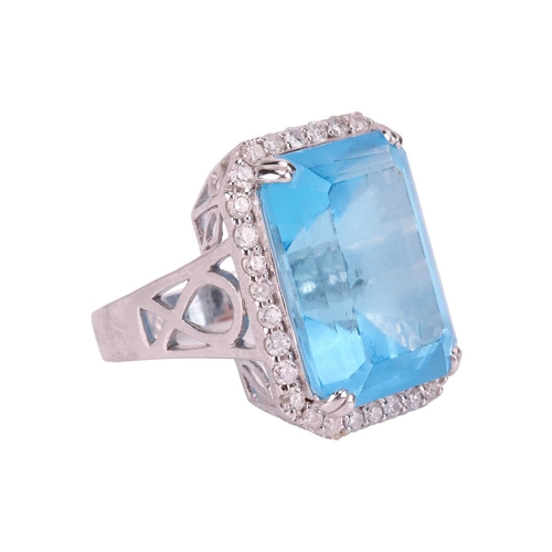 84 - A large topaz and diamond halo ring, featuring a large rectangular step-cut Swiss blue topaz with ca... 