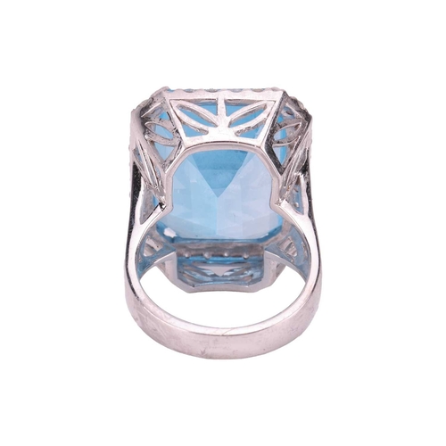 84 - A large topaz and diamond halo ring, featuring a large rectangular step-cut Swiss blue topaz with ca... 