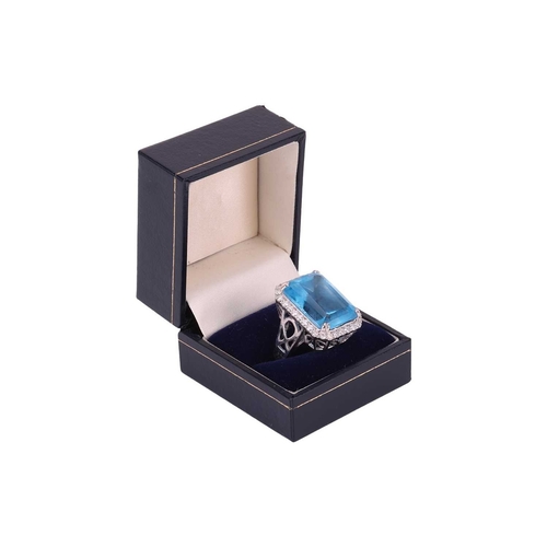 84 - A large topaz and diamond halo ring, featuring a large rectangular step-cut Swiss blue topaz with ca... 