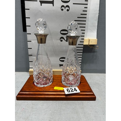 624 - Pair of cut glass decanters with silver rimmed tops on wooden base