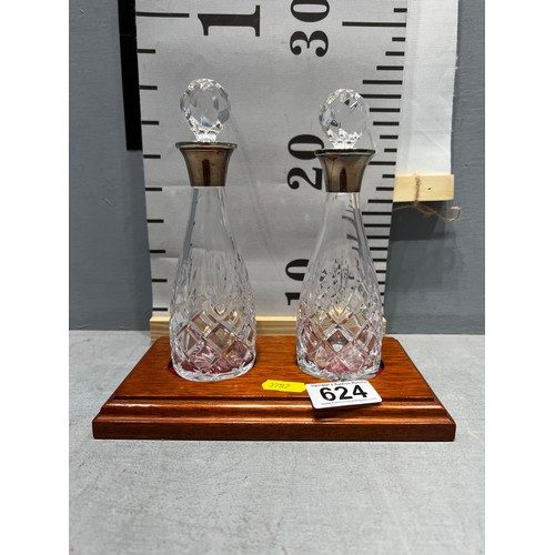 624 - Pair of cut glass decanters with silver rimmed tops on wooden base