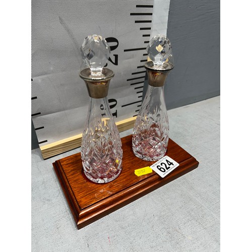 624 - Pair of cut glass decanters with silver rimmed tops on wooden base