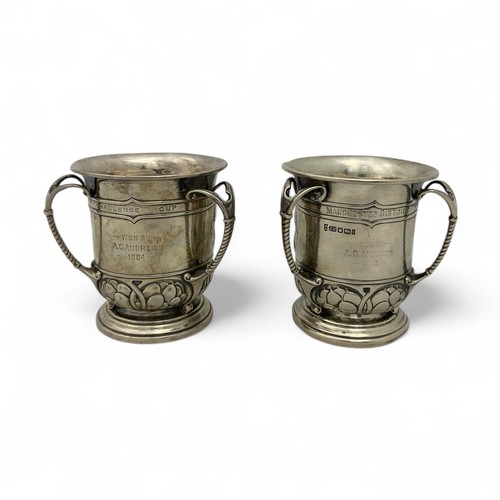 125 - Two Arts & Crafts English silver golfing trophies, in the form of three-handled mugs or tygs, em... 