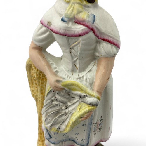 21 - A mid-late 19thC Staffordshire flatback figure of a female fishmonger, modelled holding a basket of ... 